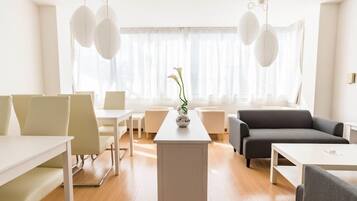 A modern hotel room with a dining area, a sofa, and a table with a vase of flowers.