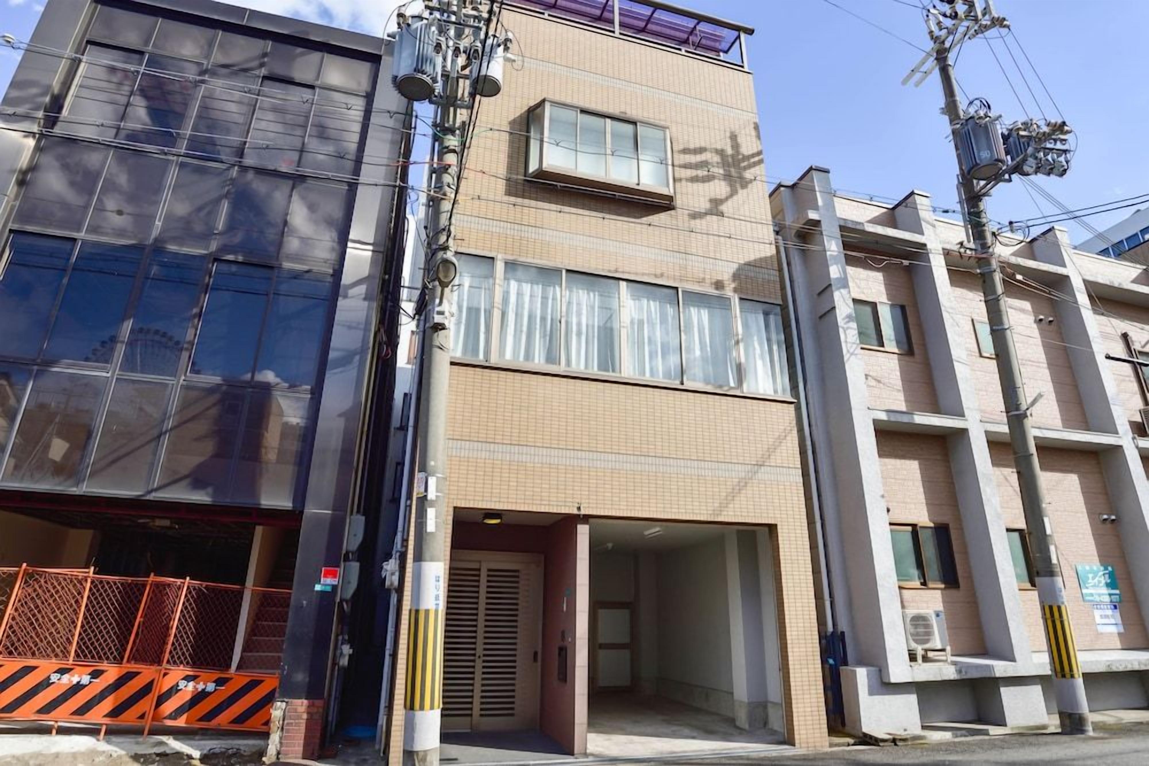 A multi-story building with a ground-level entrance, a covered area, and a visible air conditioning unit.