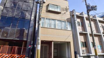 A multi-story building with a ground-level entrance, a covered area, and a visible air conditioning unit.