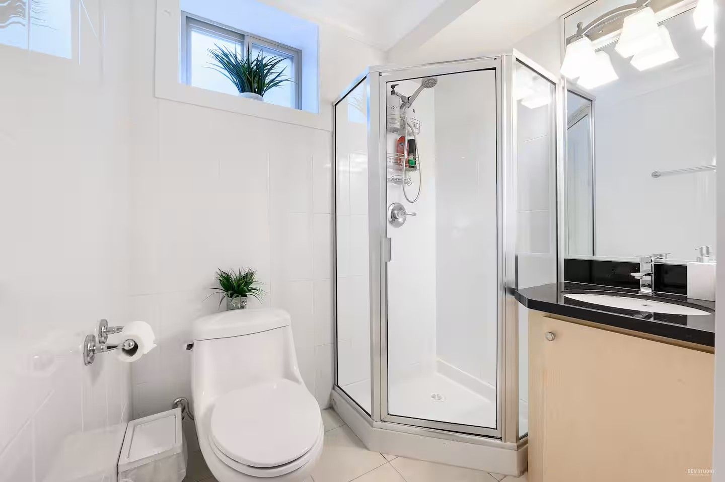 A modern bathroom with a glass-enclosed shower, a toilet, and a sink with a black countertop.