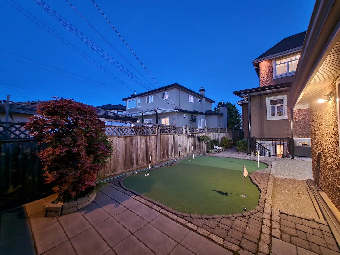 A backyard with a putting green, a wooden fence, and houses in the background.