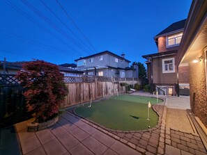 A backyard with a putting green, a wooden fence, and houses in the background. - Two bedrooms basement suite (Vancouver)