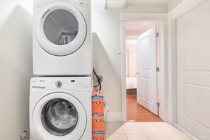 A laundry room with stacked washers and dryers, a tiled floor, and a hallway leading to a bedroom. - Two bedrooms basement suite (Vancouver)