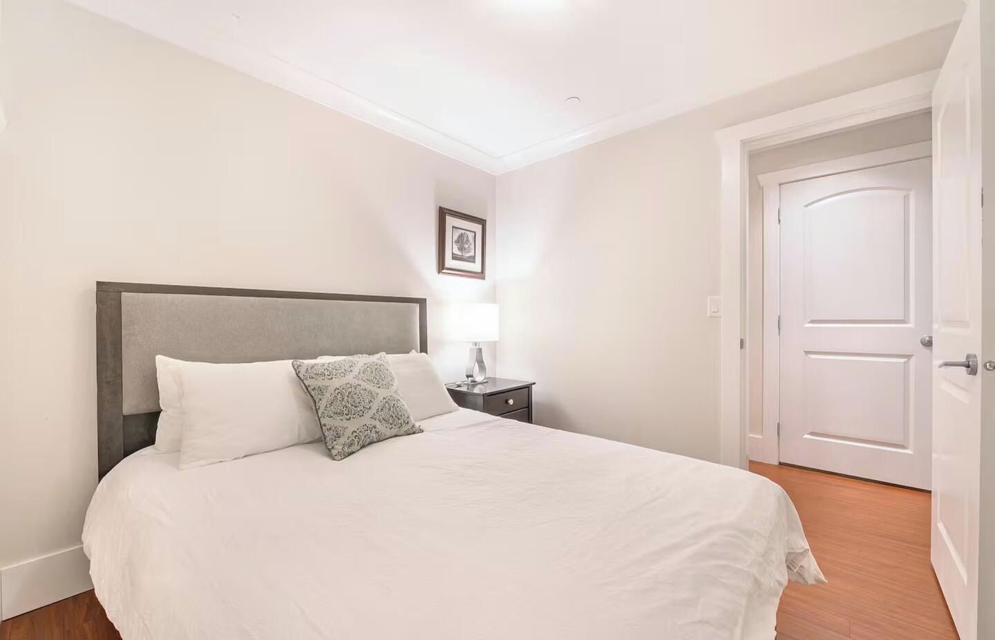 A bedroom with a bed, a nightstand, a lamp, and a door.
