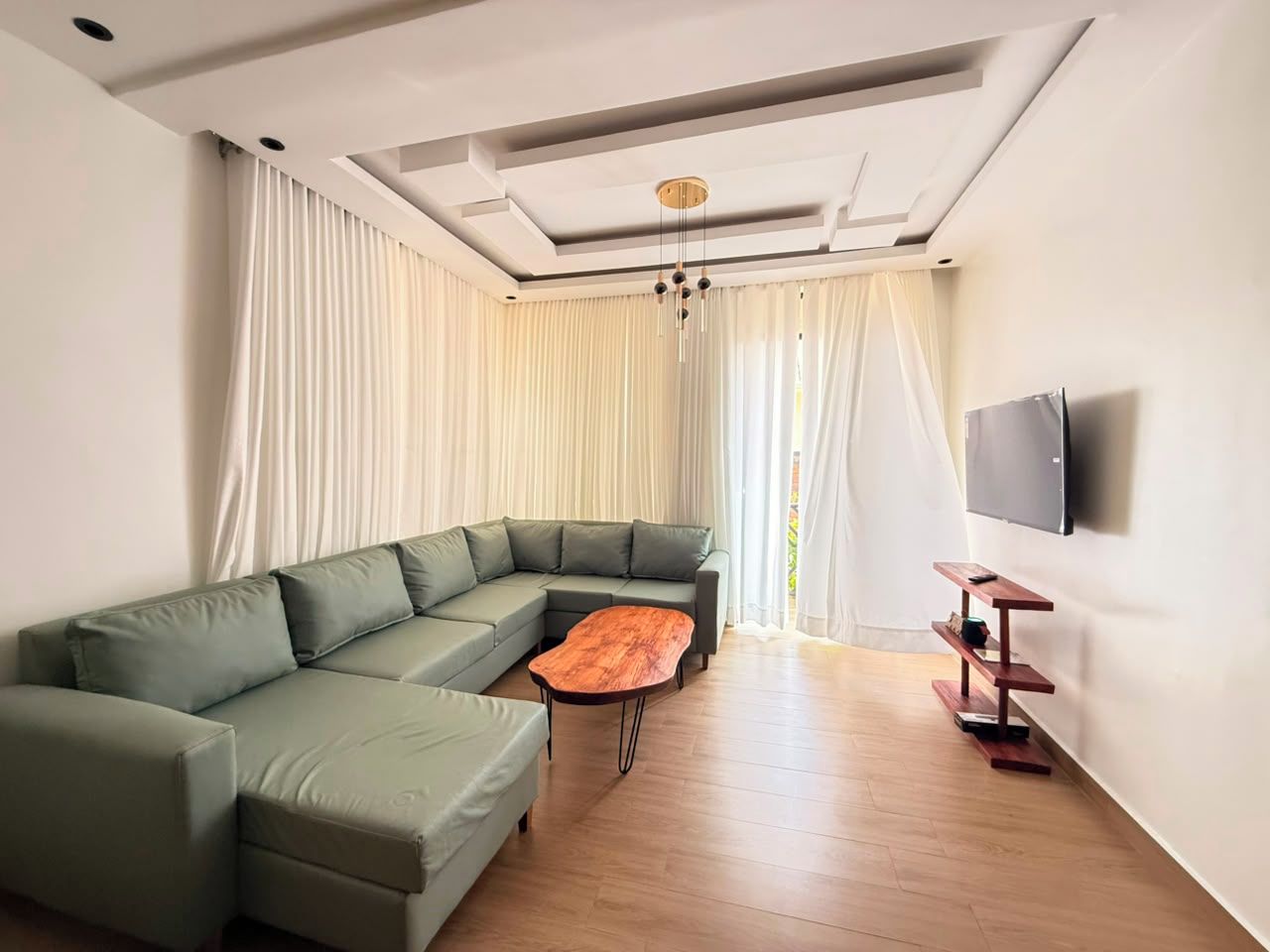 A modern living room with a sectional sofa, a wooden coffee table, and a TV on the wall.