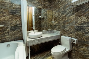 Un baño con pared de mármol, lavamanos blanco, inodoro y bañera.