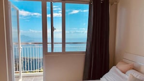 A hotel room with a bed, a view of the sea, and a balcony with a railing. - Smdc Wind Residences by Bem (Tagaytay)