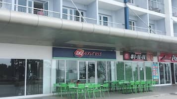 A multi-story building with a DQ Express restaurant on the ground floor, green chairs outside, and a Pizza Hut across the street.