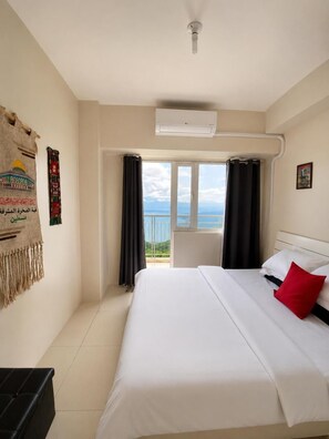 A hotel room with a bed, a ceiling fan, an air conditioning unit, a balcony with curtains, and a wall with a decorative tapestry. - Smdc Wind Residences by Bem (Tagaytay)