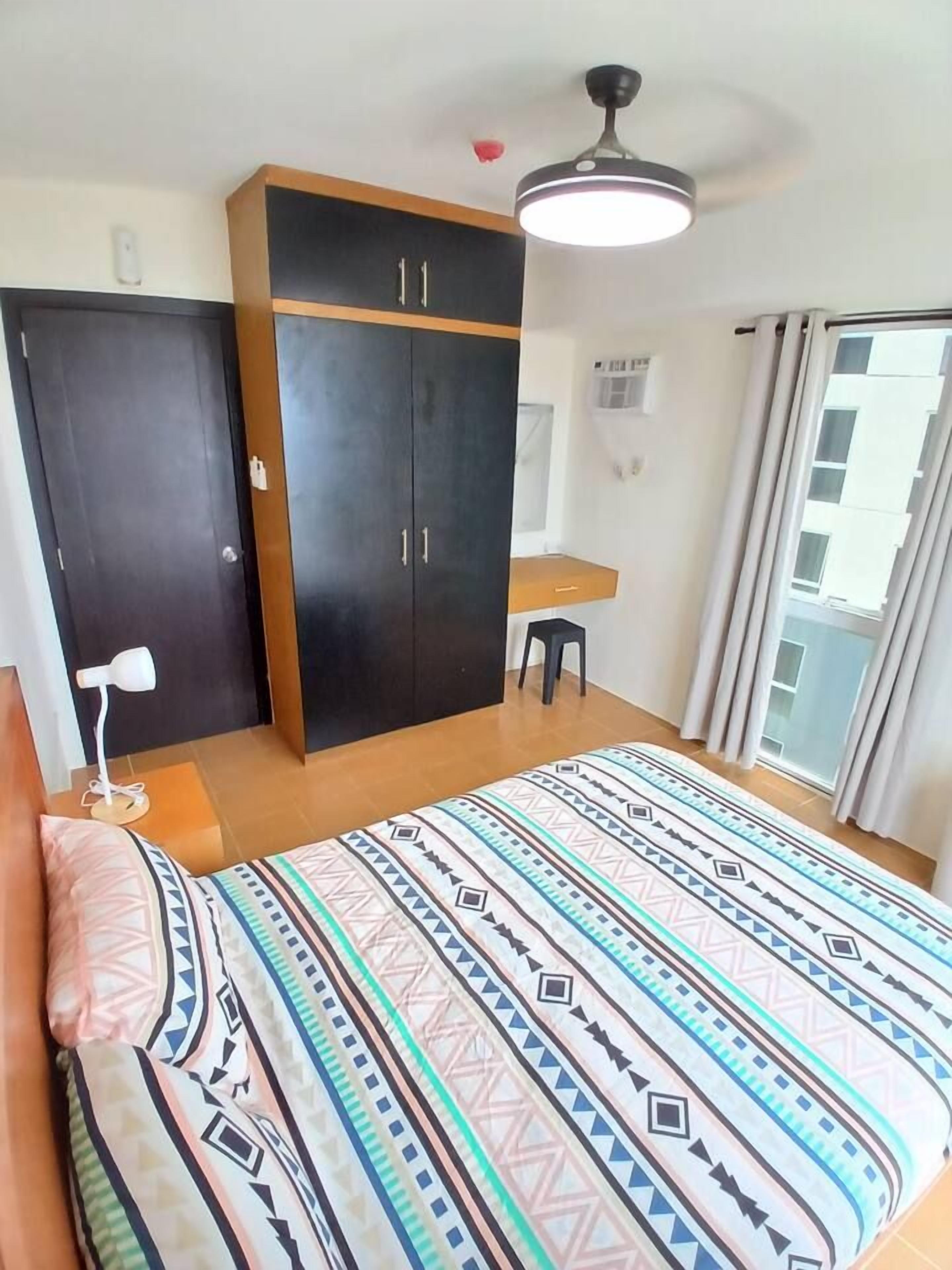 A bedroom with a bed, wardrobe, desk, and a view of the outside.