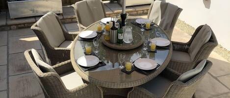 Une table de jardin ronde, avec six chaises, un grand parasol et un plateau en verre.