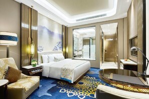A hotel room with a large bed, a sitting area, a desk, and a bathroom. - Wanda Vista Urumqi (Ürümqi)