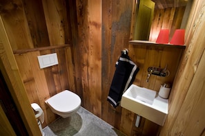 A small, wooden-paneled bathroom with a toilet, sink, and mirror. - Chalet Z'gogwärgji (Zermatt)