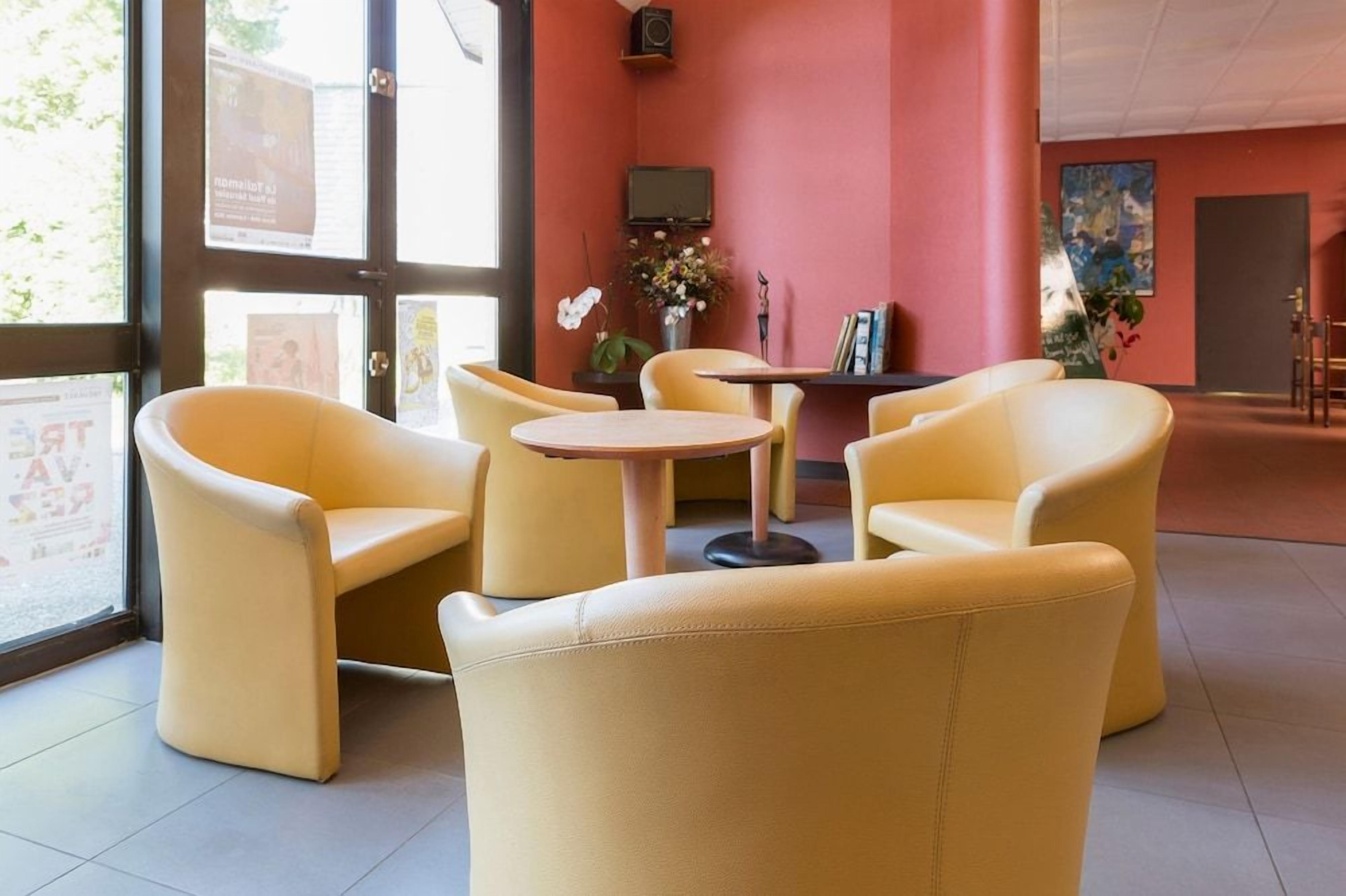 A room with yellow chairs and a small table, a television on the wall, and a window with a view.