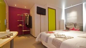 A hotel room with a bed, a TV, a coat rack, and a desk.