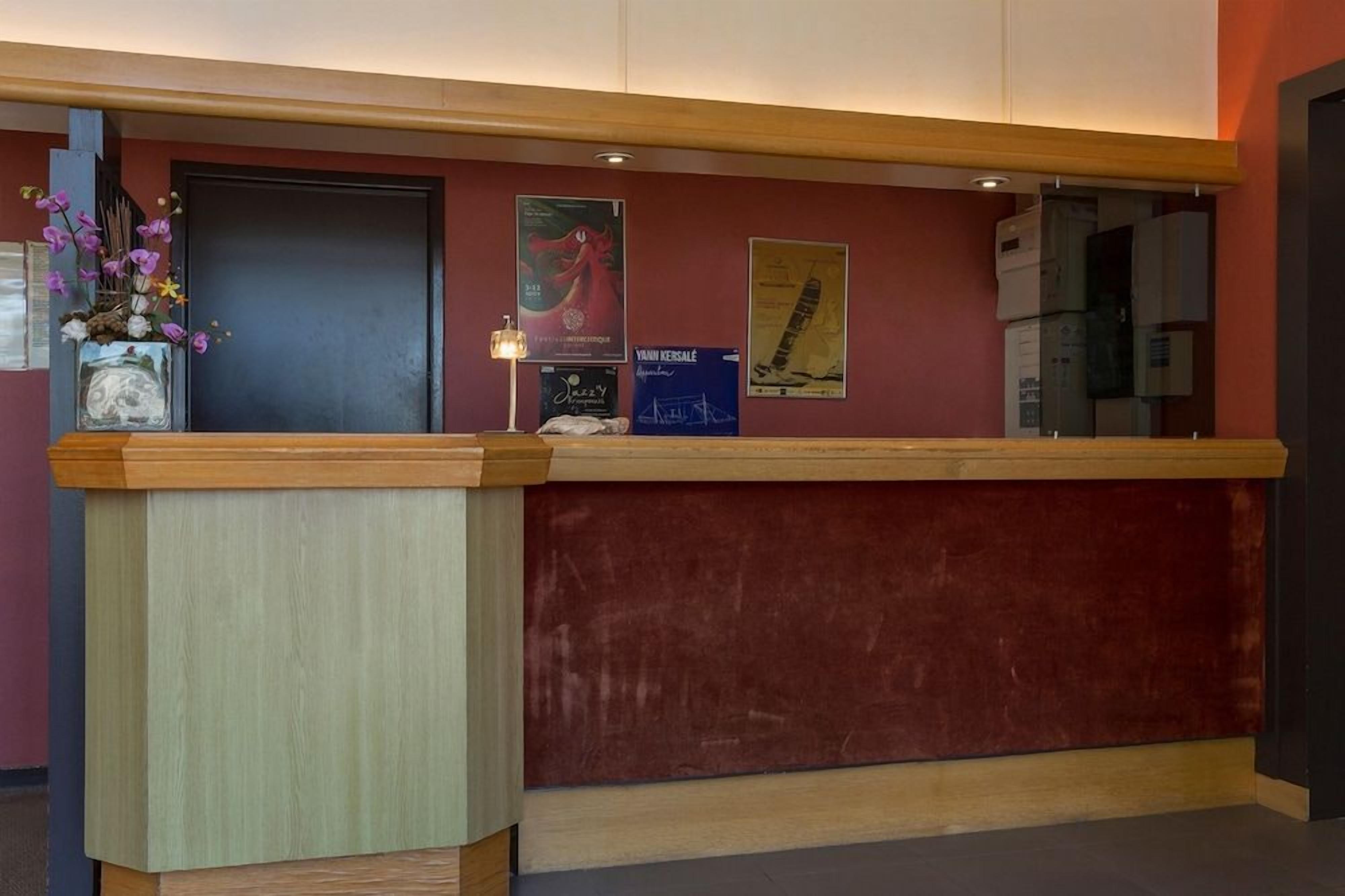 A reception desk with a wooden counter, a vase of flowers, and posters on the wall.