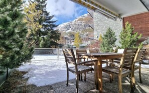 Area salotto esterna con tavolo e sedie, affacciata su un paesaggio montano innevato.