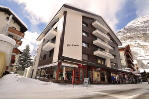 Un hotel a più piani con balconi, un cartello con su scritto 'Villa Emeline' e una strada coperta di neve.