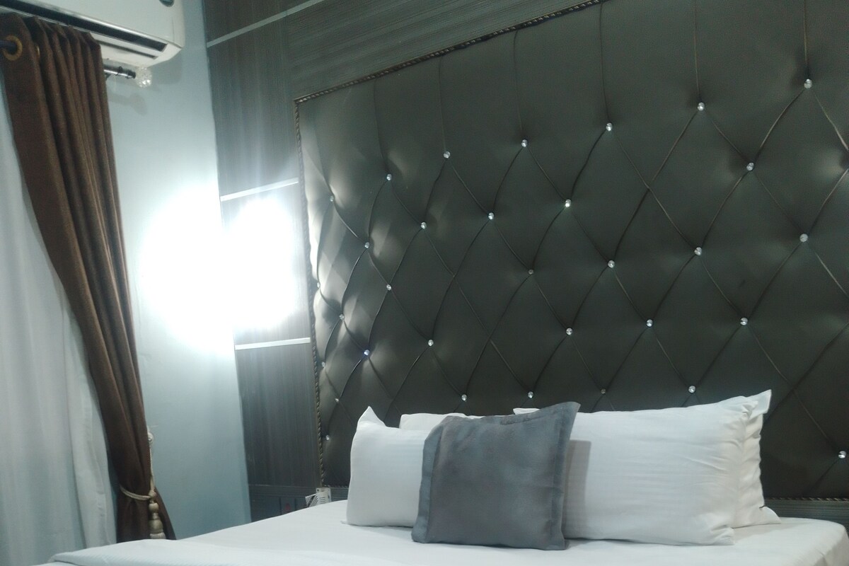 Een hotelkamer met een groot bed, een hoofdeinde met een ruitpatroon en een raam met gordijnen.
