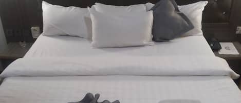 A neatly made bed with white linens, a dark headboard, and a folded towel on the bed.