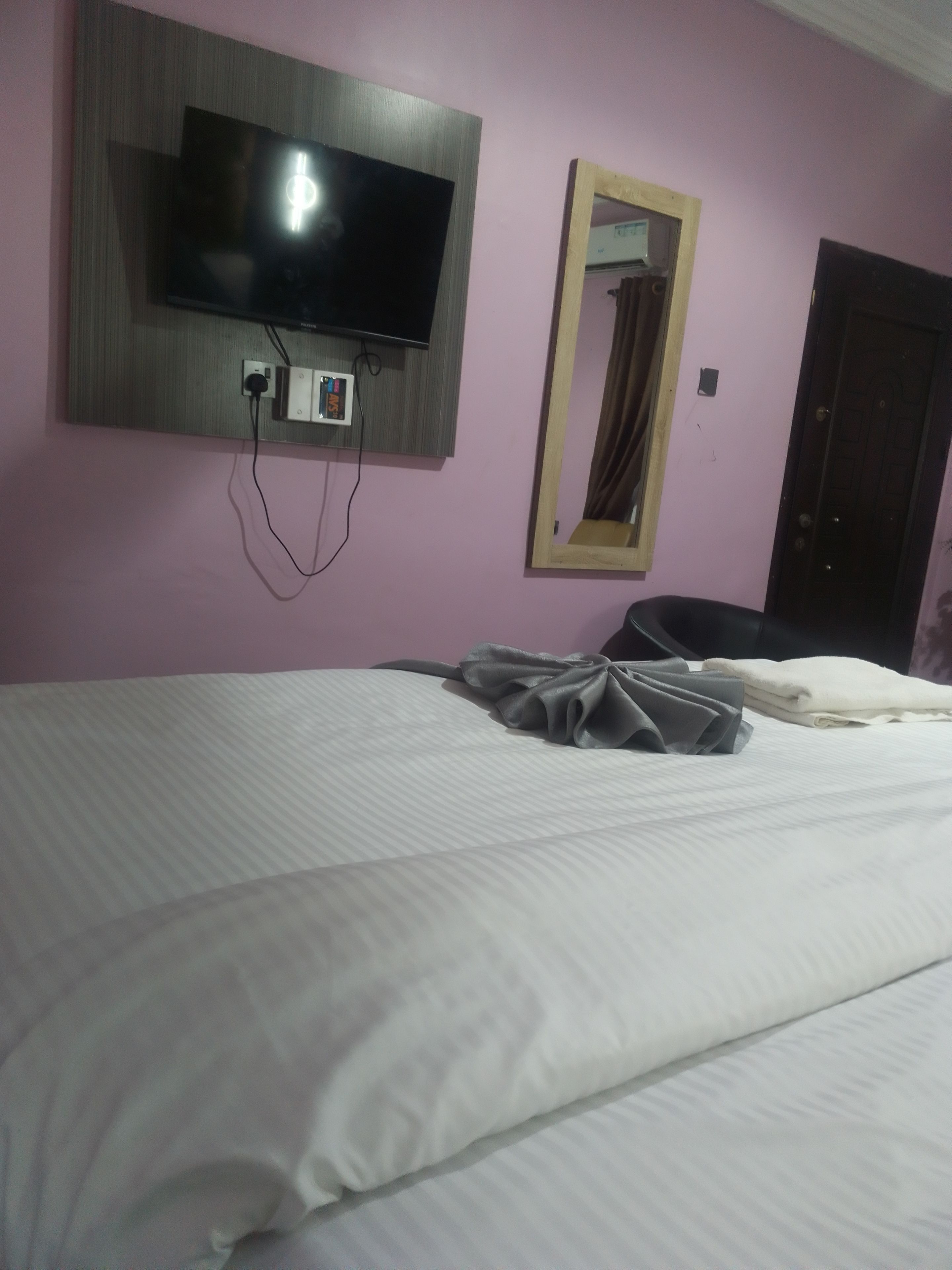 A hotel room with a bed, a flat-screen TV mounted on the wall, a mirror, and a door.