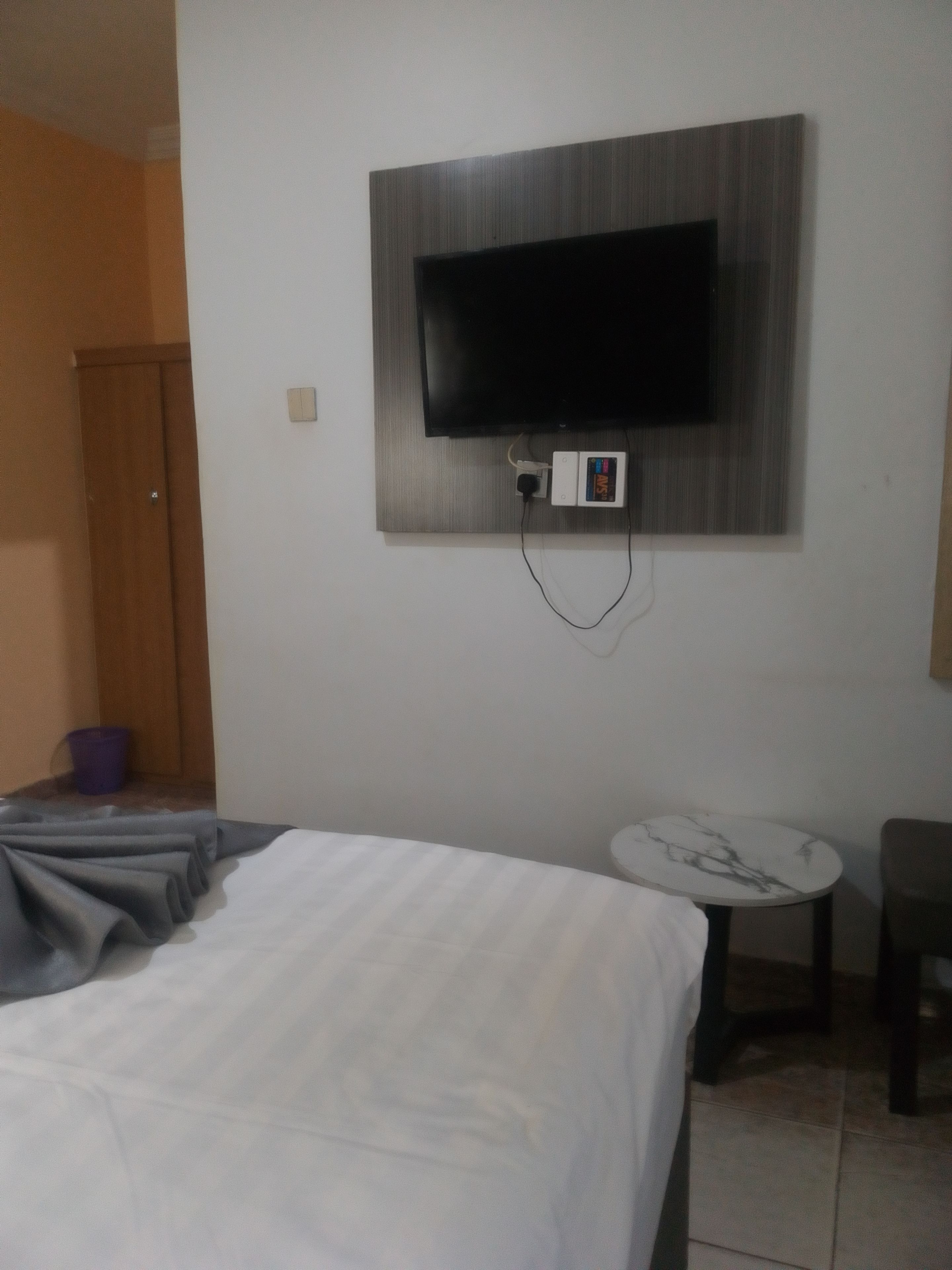Habitación de hotel con cama, una mesita redonda, televisor montado en la pared y una puerta de madera.