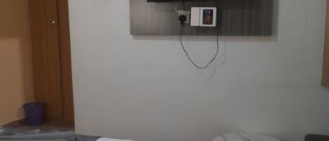 A hotel room with a bed, a small round table, a television mounted on the wall, and a wooden door.