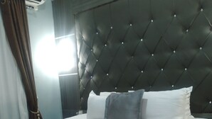 A hotel room with a large bed, a headboard with a diamond pattern, and a window with curtains. - Sethhotel (Asaba)
