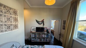 Ein Schlafzimmer mit Bett, Bücherregal, Gemälde und einem Fenster mit Vorhängen.