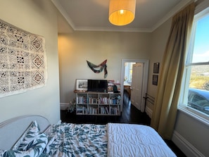 Un dormitorio con cama, una estantería, un cuadro y una ventana con cortinas.