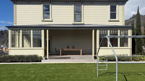 Ein zweistöckiges Haus mit überdachter Veranda, einem Tisch mit Stühlen und einer Metall-Schaukel.