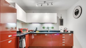 A kitchen with red cabinets, a microwave, a toaster, and a clock on the wall.