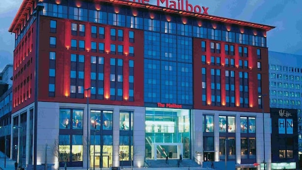 A modern building with 'The Mailbox' signage, featuring a prominent entrance with glass doors and a staircase leading up to the main entrance.