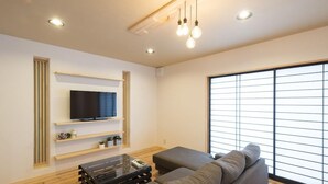 Un salon moderne avec un téléviseur à écran plat, des étagères en bois, un canapé et une grande fenêtre.