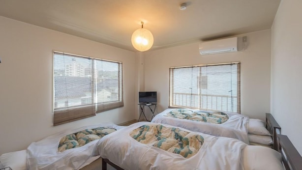 Une chambre d’hôtel avec deux lits, de grandes fenêtres, un téléviseur à écran plat et un luminaire au plafond.