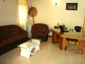 A living room with a sofa, armchair, glass coffee table, and a wooden desk with a computer. - Layathraa Hotel and Restaurant (Kandy)