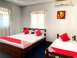 A hotel room with two beds, each with a wooden frame and red and white bedding. There is a window with a curtain, and a wall-mounted air conditioning unit. - Layathraa Hotel and Restaurant (Kandy)