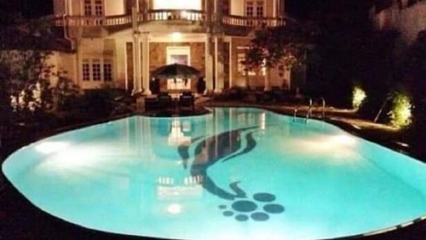 Una gran piscina il·luminada amb un disseny singular davant d'un edifici de diversos pisos de nit.