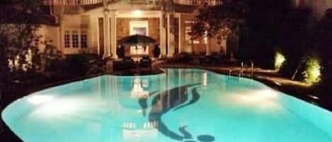 Una piscina grande e iluminada con un diseño único por la noche.
