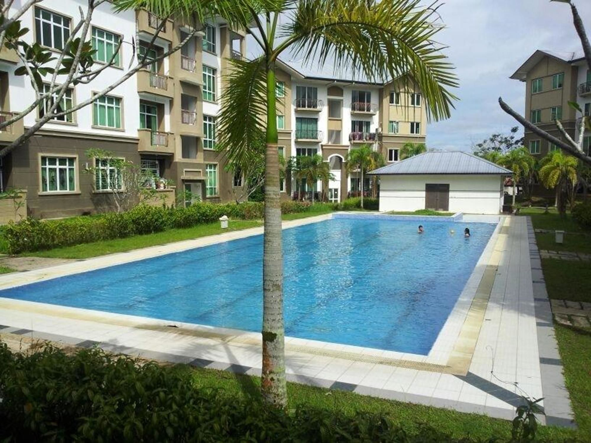 A rectangular swimming pool surrounded by a paved walkway, with a multi-story building in the background.