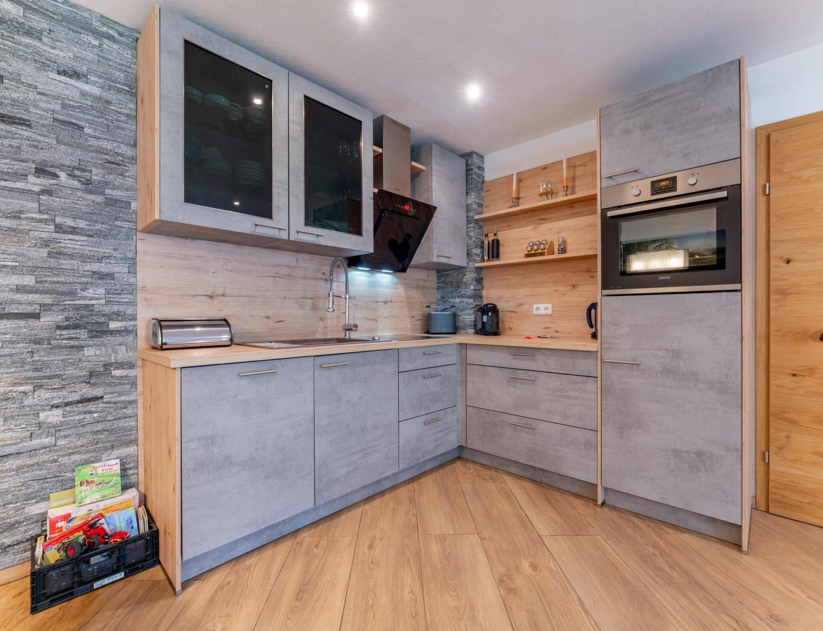 Une cuisine moderne avec des meubles gris, un four encastré et un plan de travail en bois.