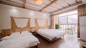 Une chambre avec deux lits, des poutres apparentes en bois au plafond, une grande fenêtre et une vue sur les bâtiments environnants.