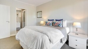 Quarto com cama, mesas de cabeceira, espelho e porta para um banheiro.
