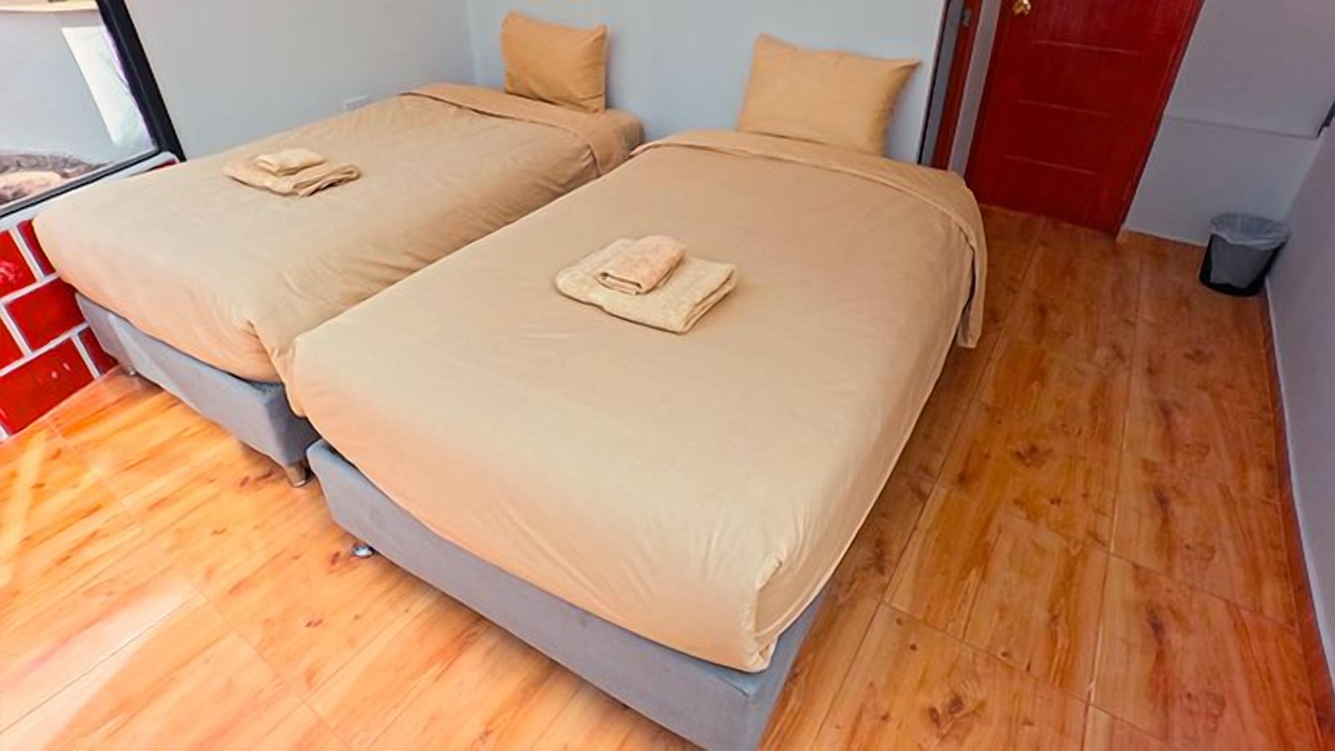 A room with two beds, each with a beige bedspread and pillows, and a wooden floor.
