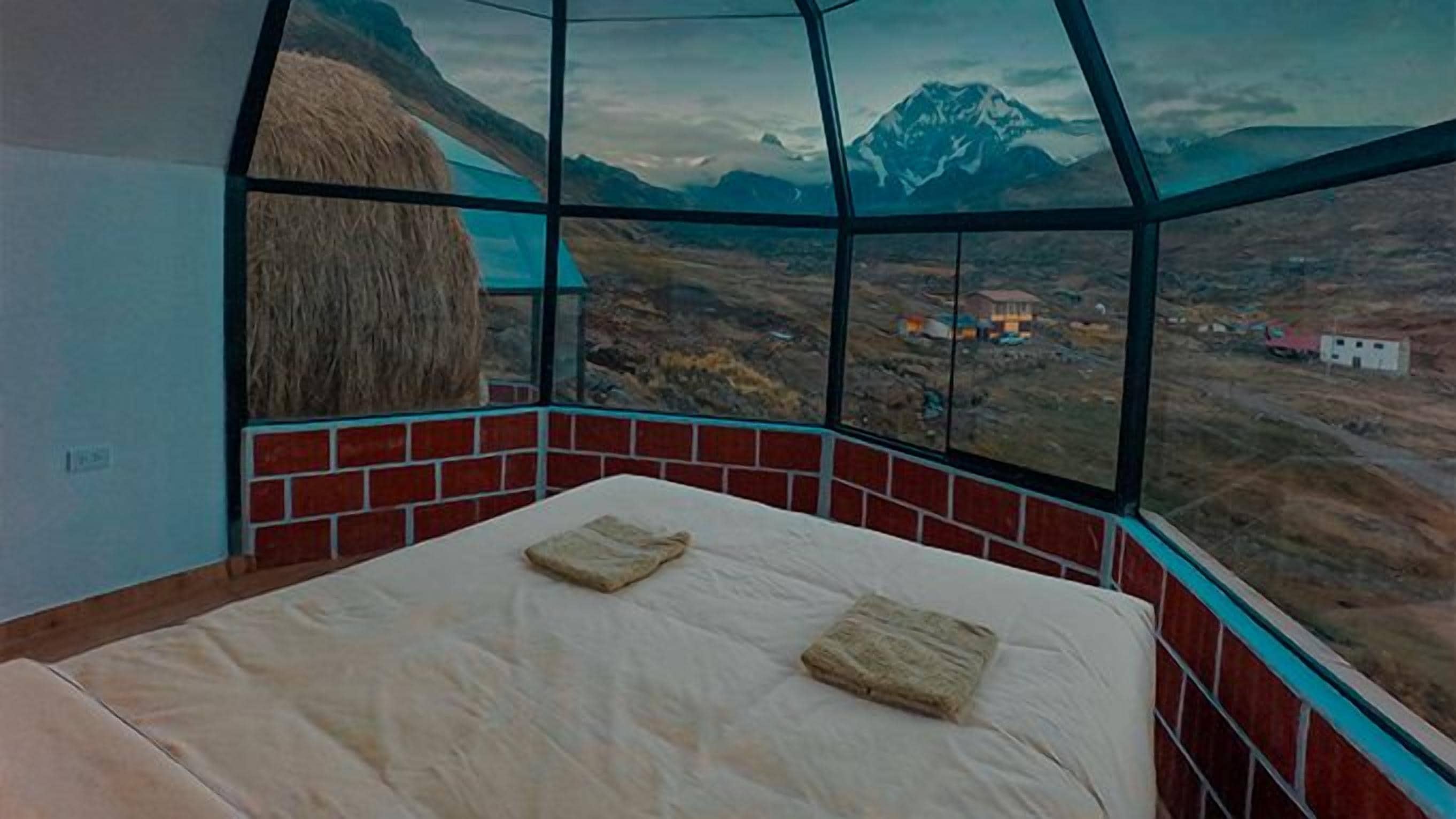 Ein Zimmer mit einem Bett, einem großen Fenster und Blick auf eine Berglandschaft.