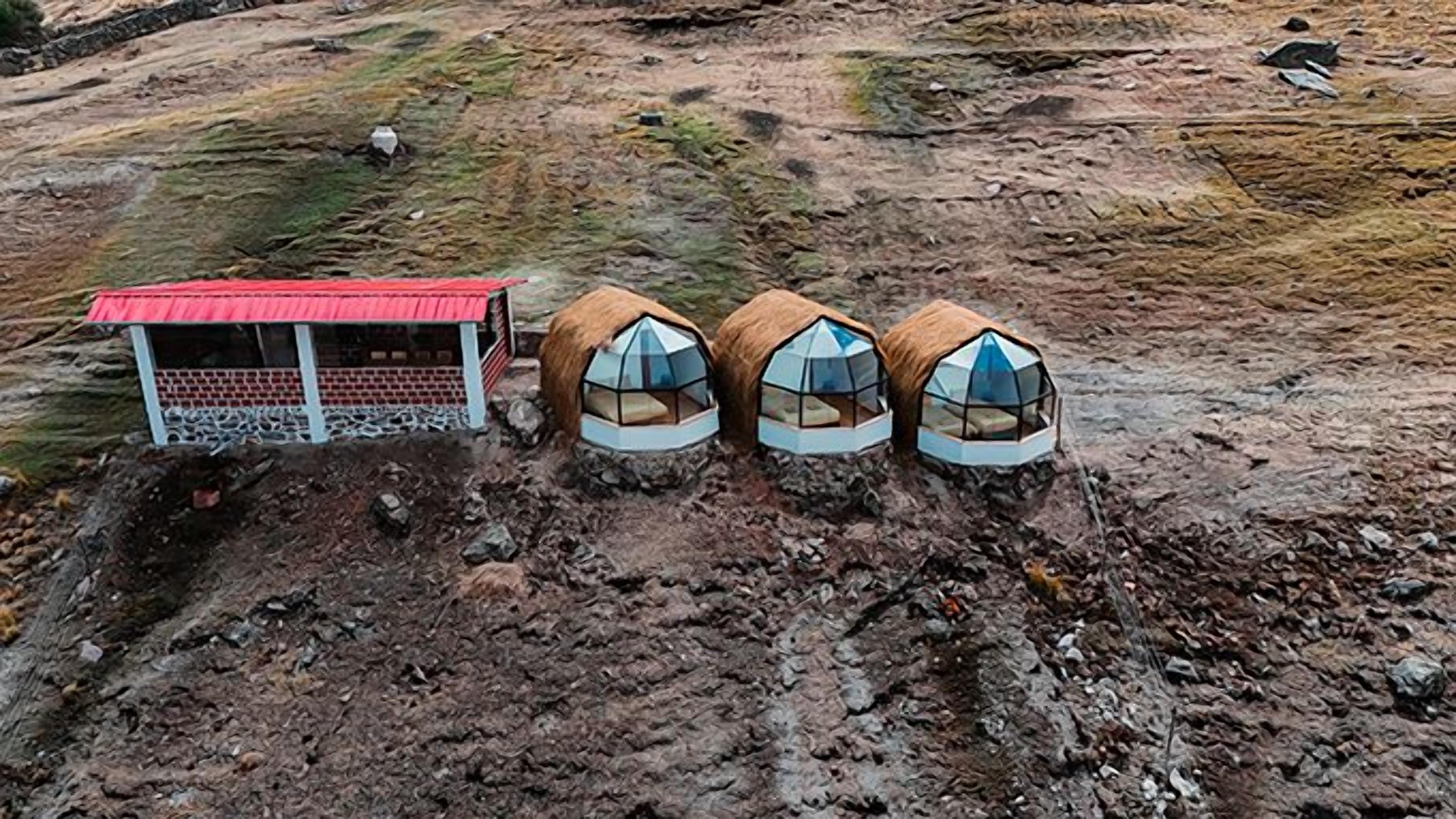 A remote, rustic accommodation with a red-roofed structure and three dome-shaped tents.