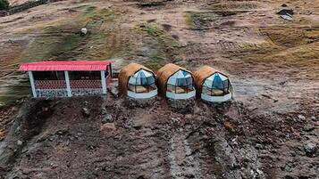 A remote, rustic accommodation with a red-roofed structure and three dome-shaped tents.