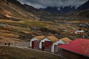 Paisagem montanhosa com um conjunto de edifícios com paredes de tijolos avermelhados e telhados de palha.