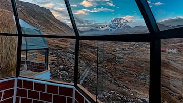 Een kamer met uitzicht op een bergachtig landschap, een bakstenen muur en een glazen wand.