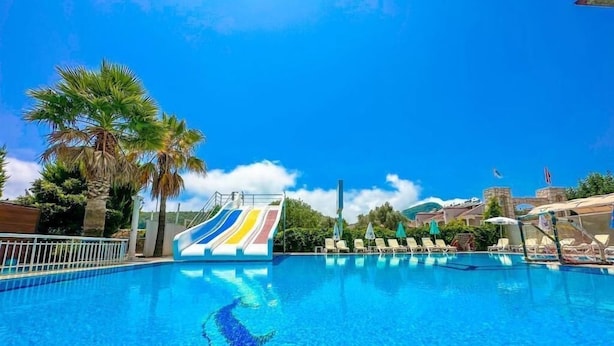A swimming pool with a water slide, palm trees, and lounge chairs. - Zehra Hotel - All Inclusive (Fethiye)